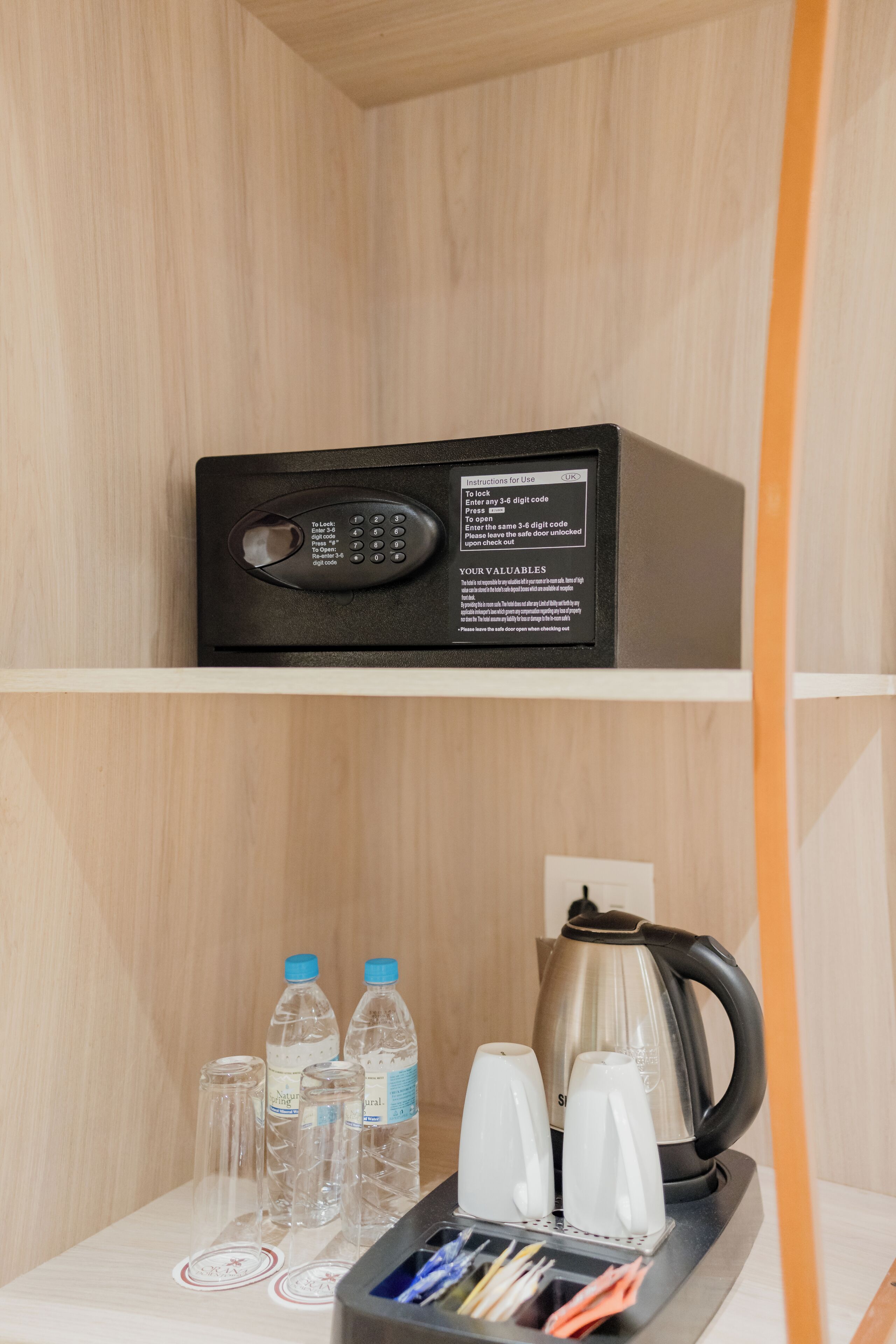 A black electronic device on a shelf with a control panel, water bottles, glasses, and a kettle.
