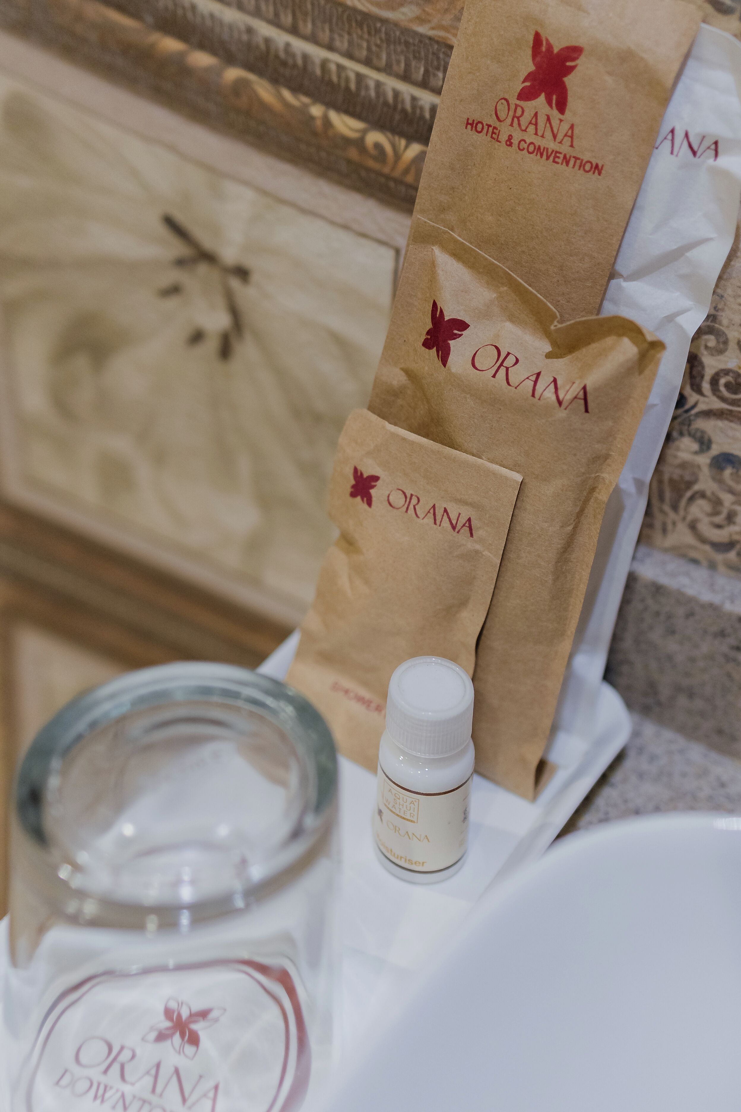 A bathroom with a marble sink, a bottle of hand soap, and paper towels branded with 'ORANA HOTEL & CONVENTION'.