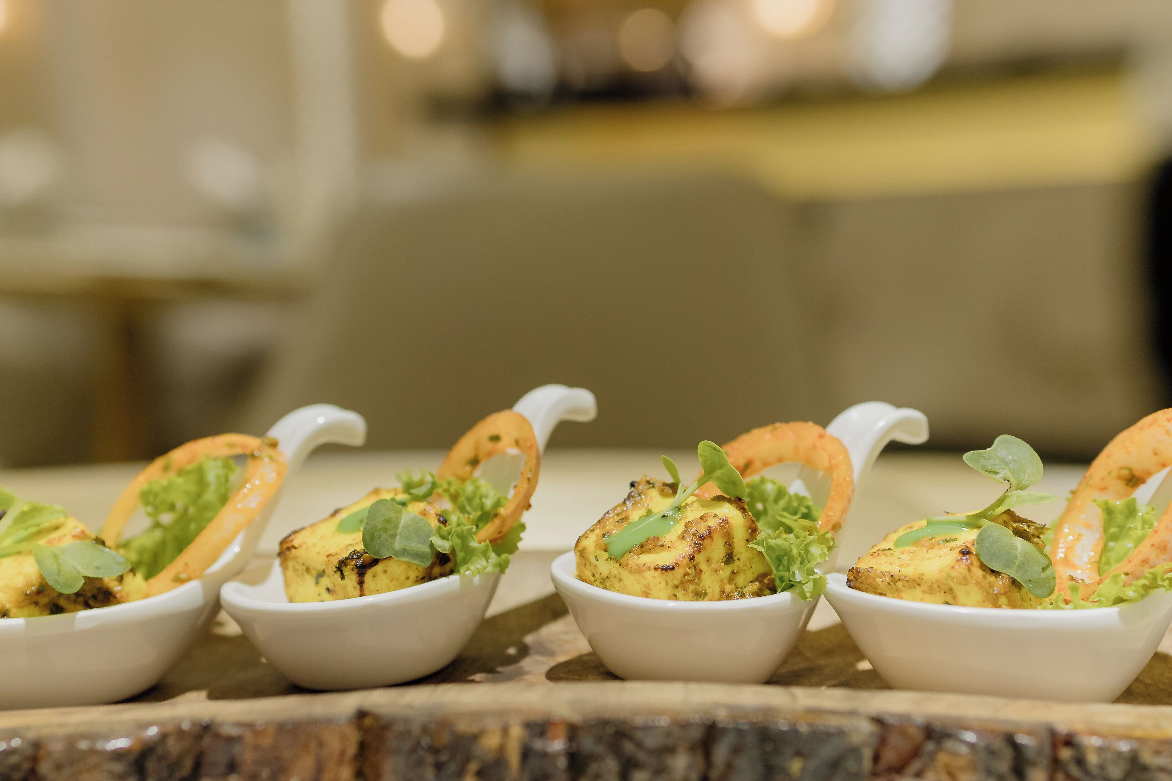Four white bowls with food garnished with greens and fried items, placed on a wooden surface.