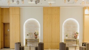 A lobby with wooden paneling, two arched niches with floral arrangements, and a ceiling with hanging spherical light fixtures. - Orana Hotel & Convention ,Vaishali 1 minute Walk from Vaishali Metro Station. (Ghaziabad)