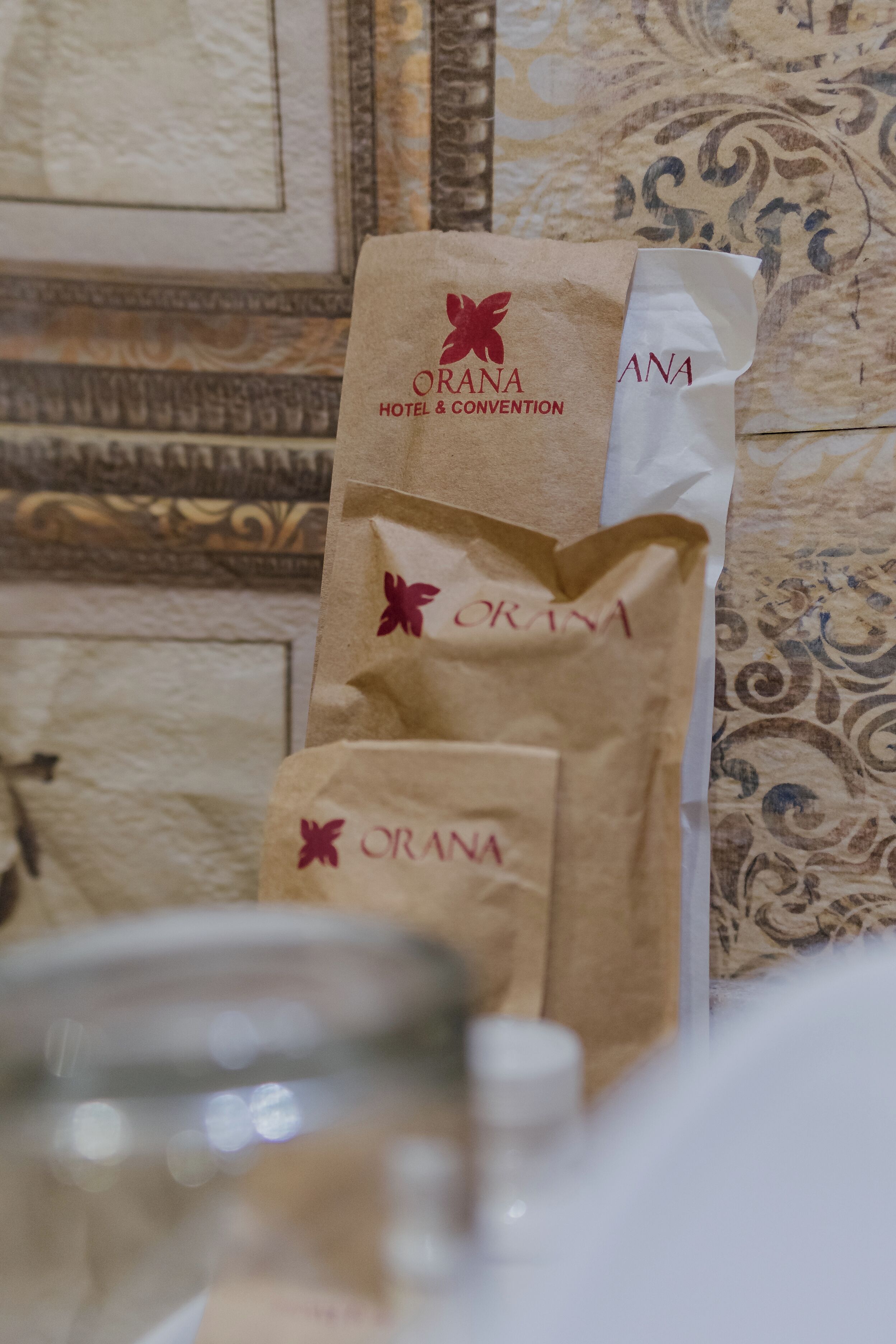 Una bolsa de papel con la leyenda 'ORANA HOTEL & CONVENTION' impresa, sobre una superficie estampada.