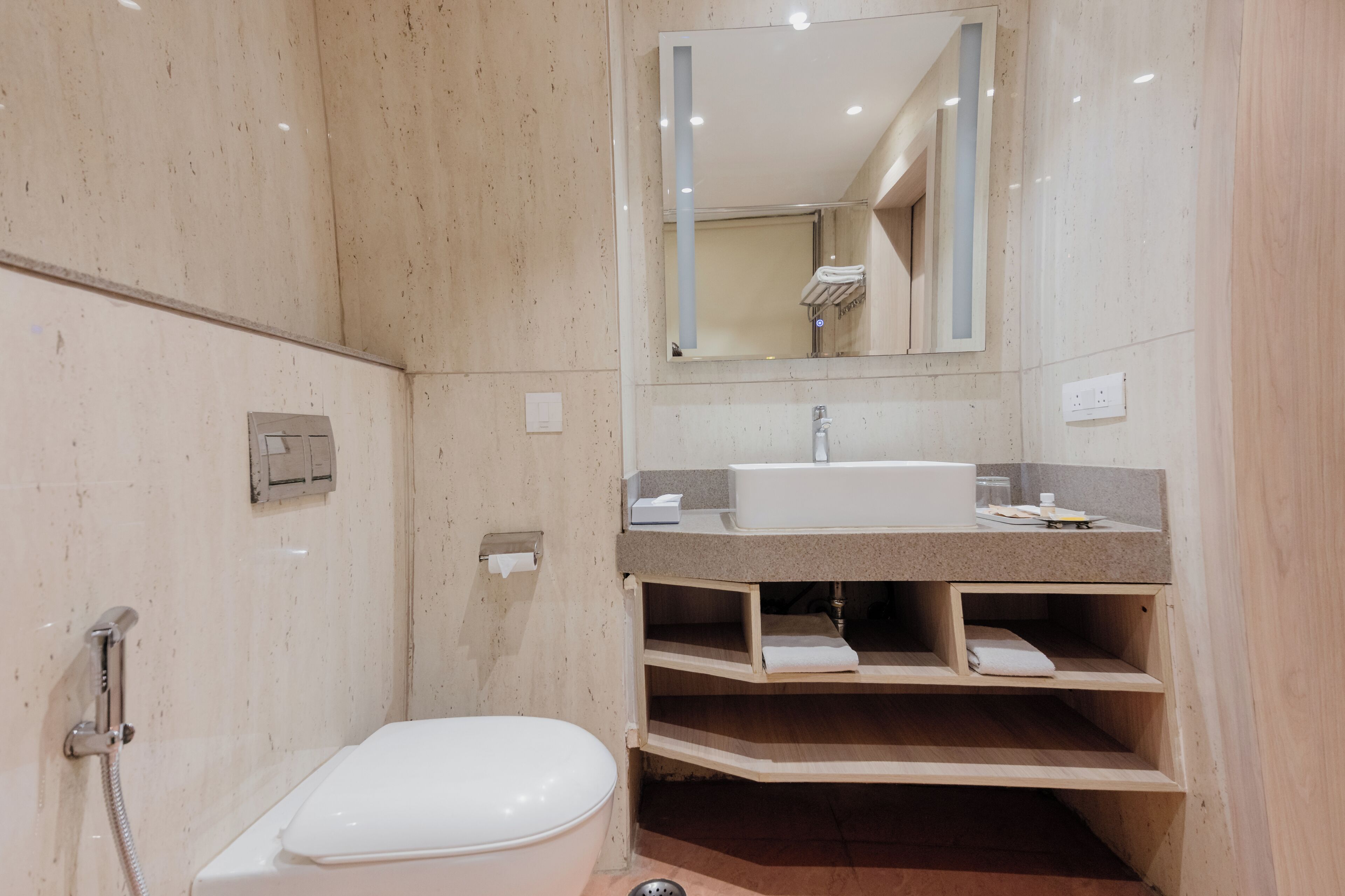 A bathroom with a toilet, sink, mirror, and shelves.