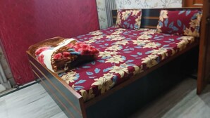 A single bed with a floral bedspread, a pillow, and a blanket. - Dev Inn Atithi Grih (Varanasi)