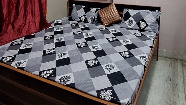 Une chambre à coucher comprenant un lit, un ventilateur de plafond, un appareil de climatisation, une fenêtre avec des rideaux et une étagère fixée au mur, ornée d’objets décoratifs.