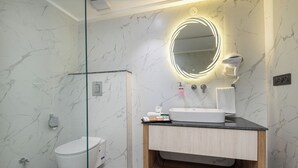 Un baño moderno con pared de mármol, un espejo redondo con iluminación, un lavamanos blanco y una ducha.