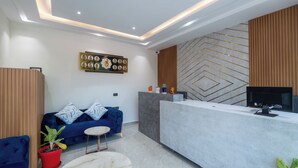 Una moderna zona de recepción con mostrador, un sofá azul, una pequeña mesa redonda y una planta en maceta.
