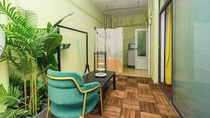 A small room with a wooden floor, a teal chair, a table with a plate, and a hanging rack.