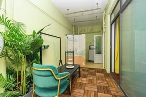 A small room with a wooden floor, a teal chair, a table with a plate, and a hanging rack. - SilkStay Apartment Chengdu Kuanzhai Alley (Chengdu)