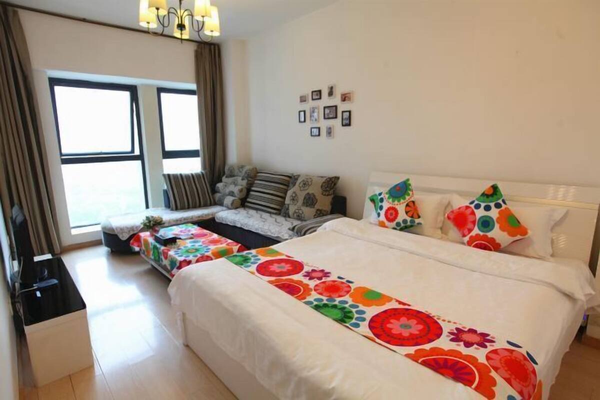 A hotel room with a large bed, a sofa, a small table, and a window with curtains.
