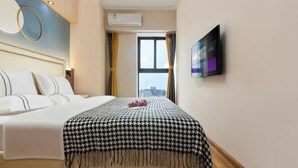 A hotel room with a bed, a television on the wall, an air conditioning unit, and a window with curtains.