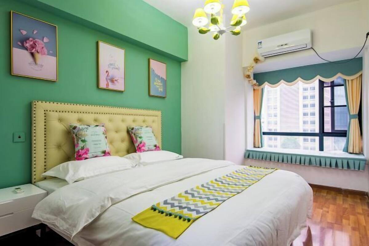 A bedroom with a bed, a bedside table, a window with curtains, and wall art.