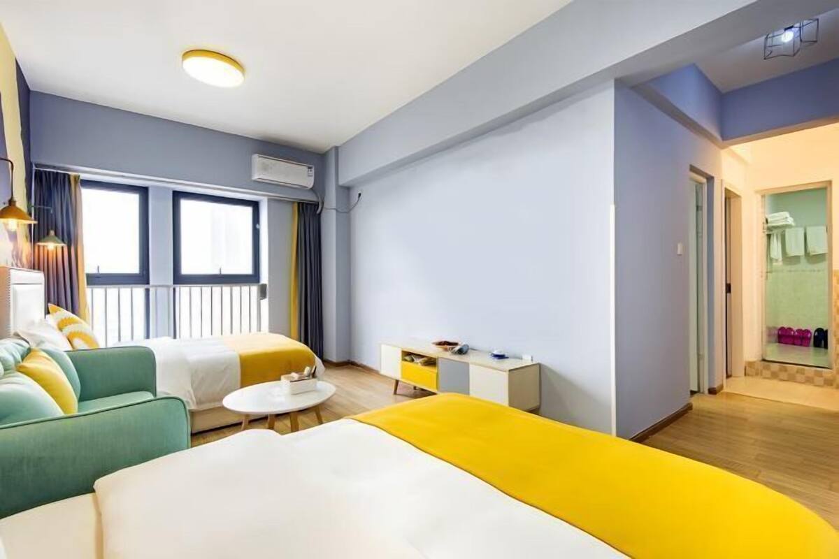 A hotel room with a bed, a sofa, a small table, and a bathroom visible through an open door.
