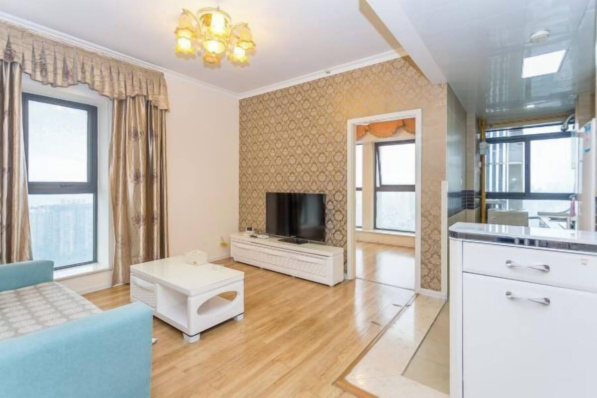 A modern living room with a TV, a sofa, a coffee table, and a kitchen area with cabinets.