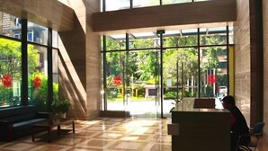 A lobby with a check-in desk, seating area, and large windows offering a view of greenery outside.