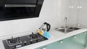 A kitchen with a gas stove, a kettle, a sink, and teal cabinets.