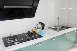 A kitchen with a gas stove, a kettle, a sink, and teal cabinets. - SilkStay Apartment Chengdu Kuanzhai Alley (Chengdu)