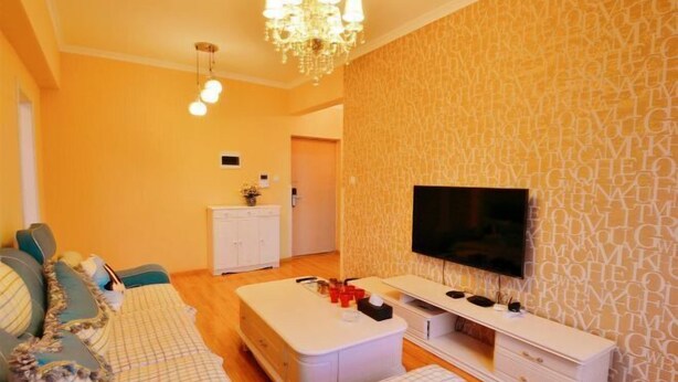 A living room with a sofa, ottoman, TV, and a patterned wall.