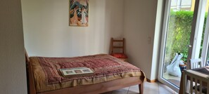 A bedroom with a bed, a chair, a window, and a painting on the wall. - Temporary apartment (Freiburg)