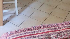 Une pièce avec une armoire blanche, un téléviseur posé sur un meuble blanc et une chaise avec un coussin.