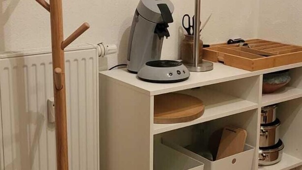 Un coin cuisine avec un porte-manteau en bois, une machine à café et un panier à fruits accroché au mur.