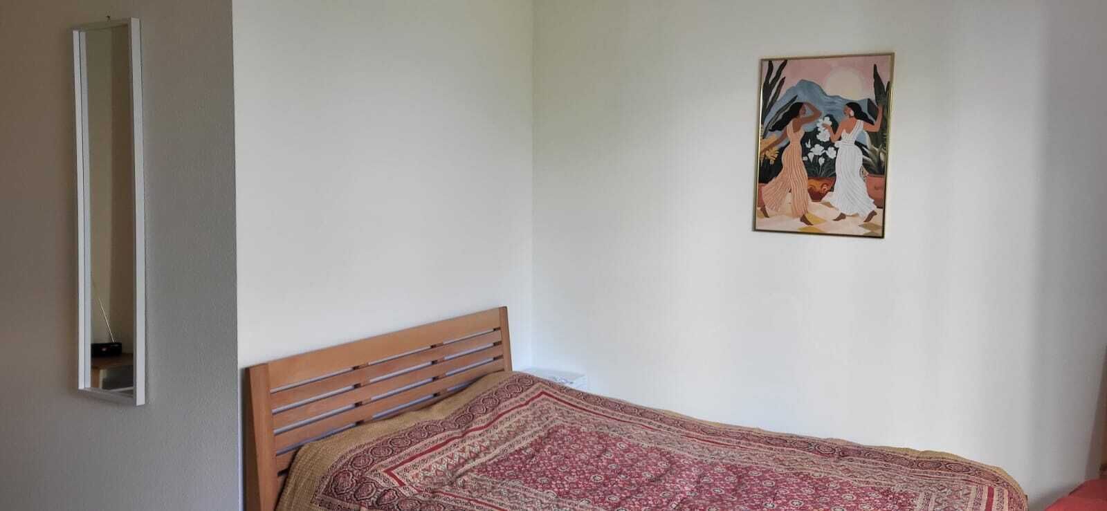 A bedroom with a wooden bed, a patterned bedspread, a wall-mounted painting, and a mirror.