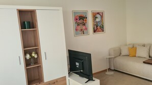 Un salon comprenant un canapé, un téléviseur, un meuble avec des étagères et deux tableaux accrochés au mur.