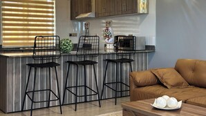 A modern kitchen with wooden cabinets, a countertop, and three black bar stools. - Vee Serviced Apartments & Hotel (Entebbe)
