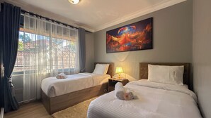 A hotel room with two beds, a painting, a window with curtains, and a rug. - Vee Serviced Apartments & Hotel (Entebbe)