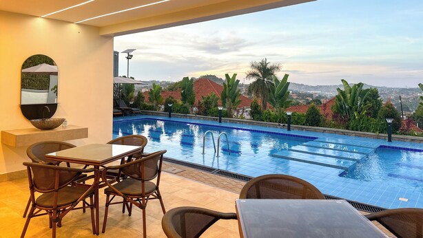 A poolside area with a view of a cityscape, a dining table with chairs, and a large mirror on the wall. - Vee Serviced Apartments & Hotel (Entebbe)