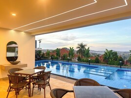 Un área junto a la piscina con vistas a un paisaje urbano, una mesa de comedor con sillas y un espejo grande en la pared.