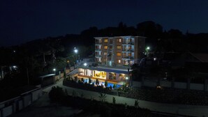 A multi-story hotel with a pool area, outdoor lighting, and a view of the surrounding landscape. - Vee Serviced Apartments & Hotel (Entebbe)