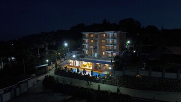 Un hotel de varios pisos con área de piscina, iluminación exterior y vistas al paisaje circundante.