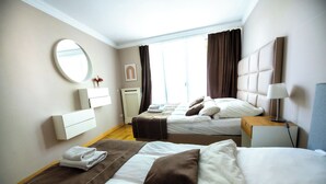 Ett hotellrum med två sängar, en rund spegel, ett sängbord med en lampa, ett element och ett fönster med gardiner.