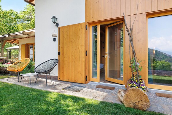 A wooden house with a sliding glass door, a small patio with a table and chairs, and a log with flowers.