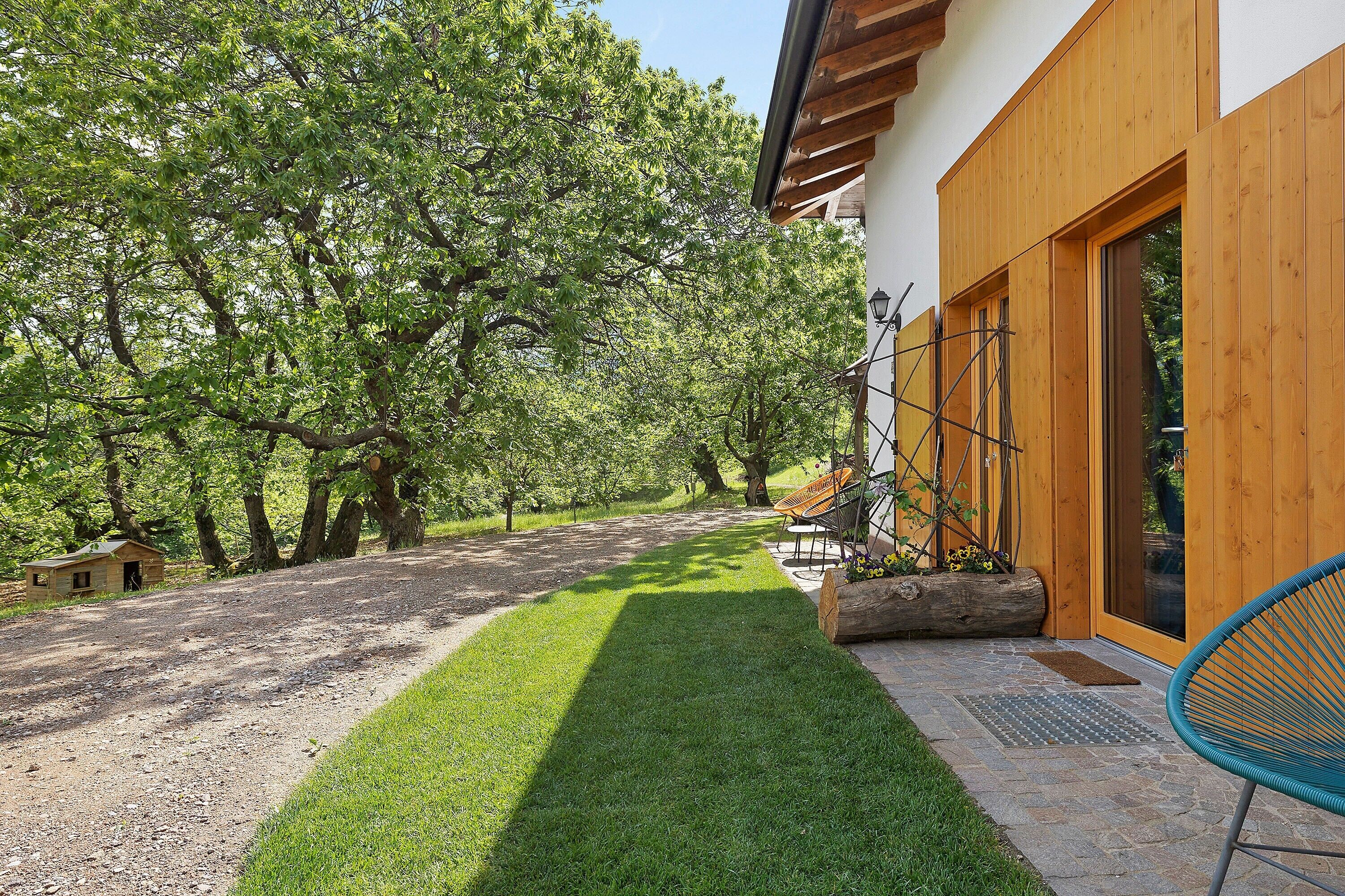 Une pelouse bien entretenue, une maison en bois avec une grande porte et un petit abri de jardin, le tout dans un cadre extérieur ensoleillé.