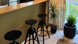 A modern kitchen with a wooden countertop, two black bar stools, a potted plant, and a clock on the wall. - Apartment in quiet, secure residence (Paimpol)