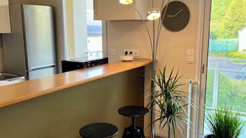 Une cuisine moderne avec un plan de travail en bois, deux tabourets de bar noirs, une plante en pot et une horloge au mur.
