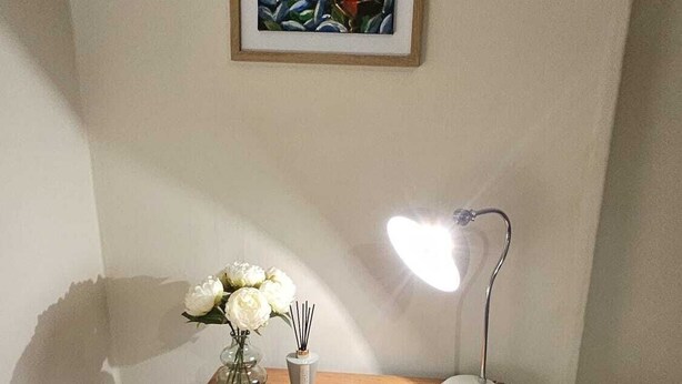 Una cassettiera in legno con cassetti, una lampada da tavolo e un vaso con fiori bianchi, tutto sullo sfondo di una parete.