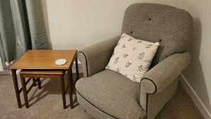 Una stanza con una poltrona grigia, un tavolino in legno e un quadro appeso al muro.