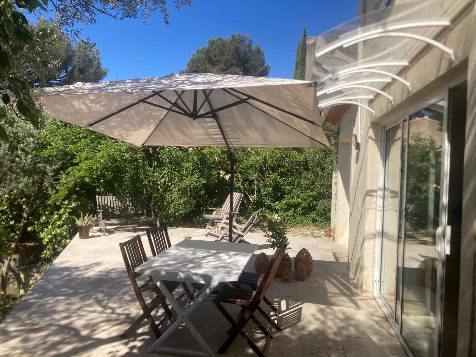 Een terras met een tafel, stoelen, een parasol en uitzicht op de groene omgeving.
