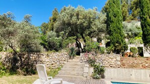Une terrasse en bois avec deux chaises longues blanches, un mur en pierre et une piscine.