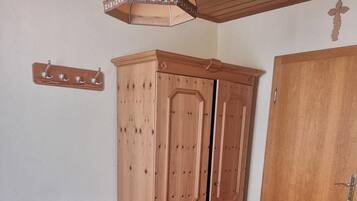 Un dormitorio con cama, armario de madera, escritorio con silla, un pequeño cubo de basura y un panel de ganchos en la pared.