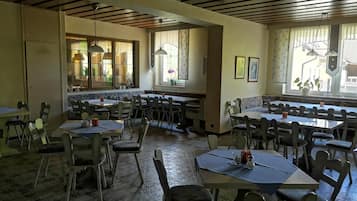A restaurant with multiple tables and chairs, a tiled floor, and large windows with curtains.