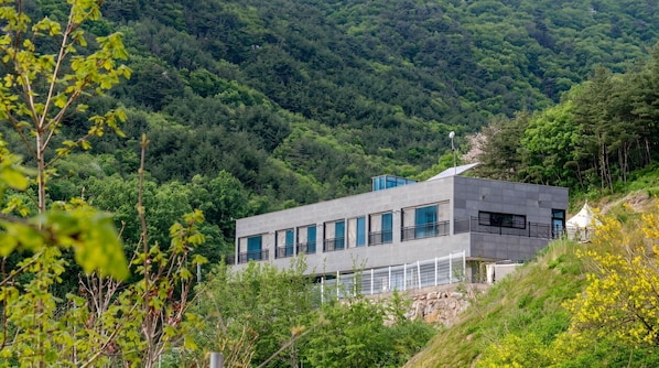 Un bâtiment moderne aux grandes fenêtres, qui se détache sur un paysage de forêt dense et de collines.