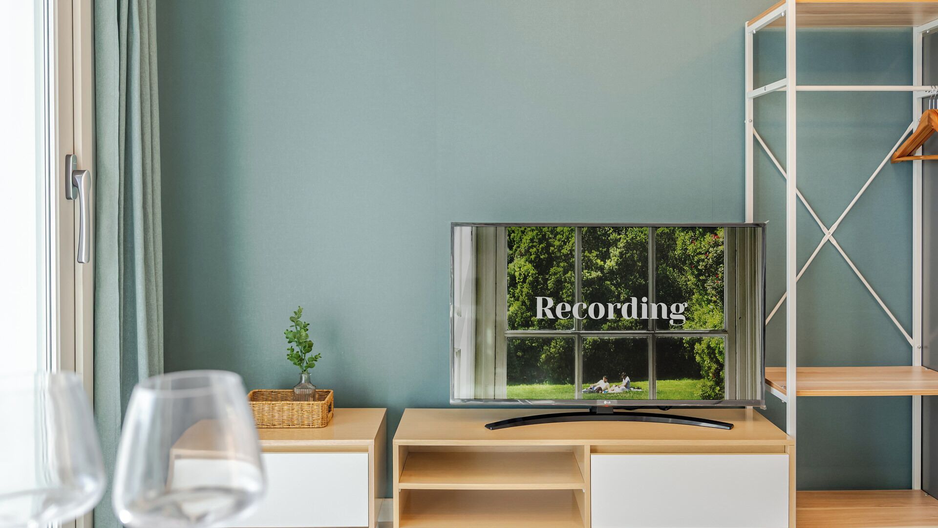 A room with a window displaying the word 'Recording,' a wooden desk, a wicker basket, and a glass of water.