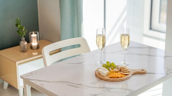 Une table en marbre avec deux coupes de champagne, une planche en bois avec du fromage et des raisins, et une chaise blanche.