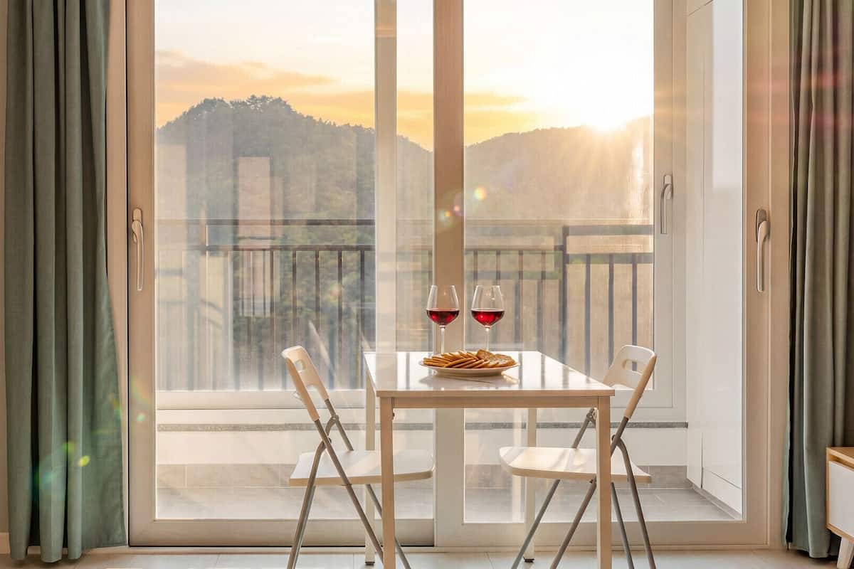 A balcony with a table and chairs, two glasses of red wine, and a plate of snacks.
