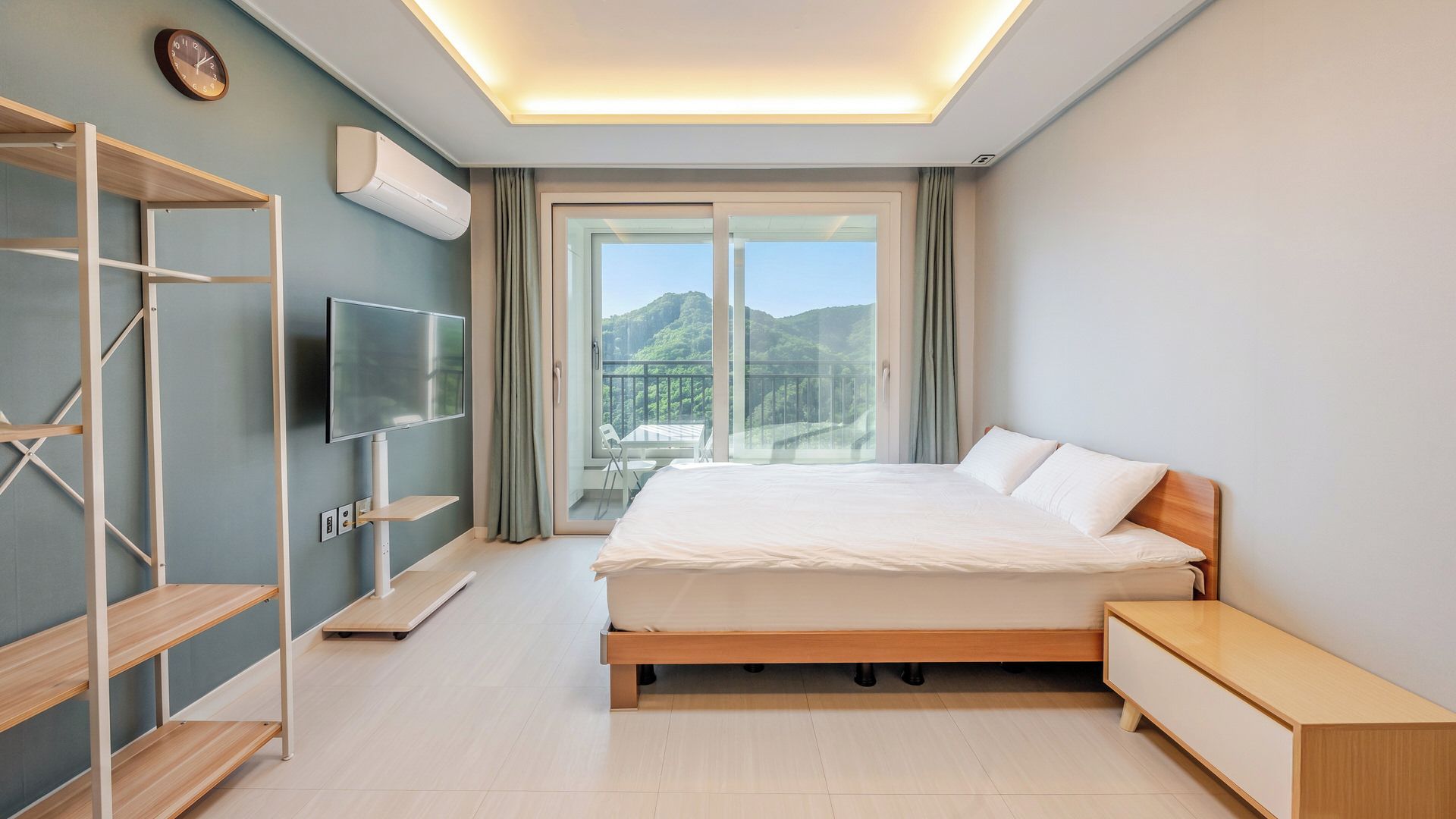 A modern hotel room with a bed, a TV, a balcony with a mountain view, and a ceiling light.