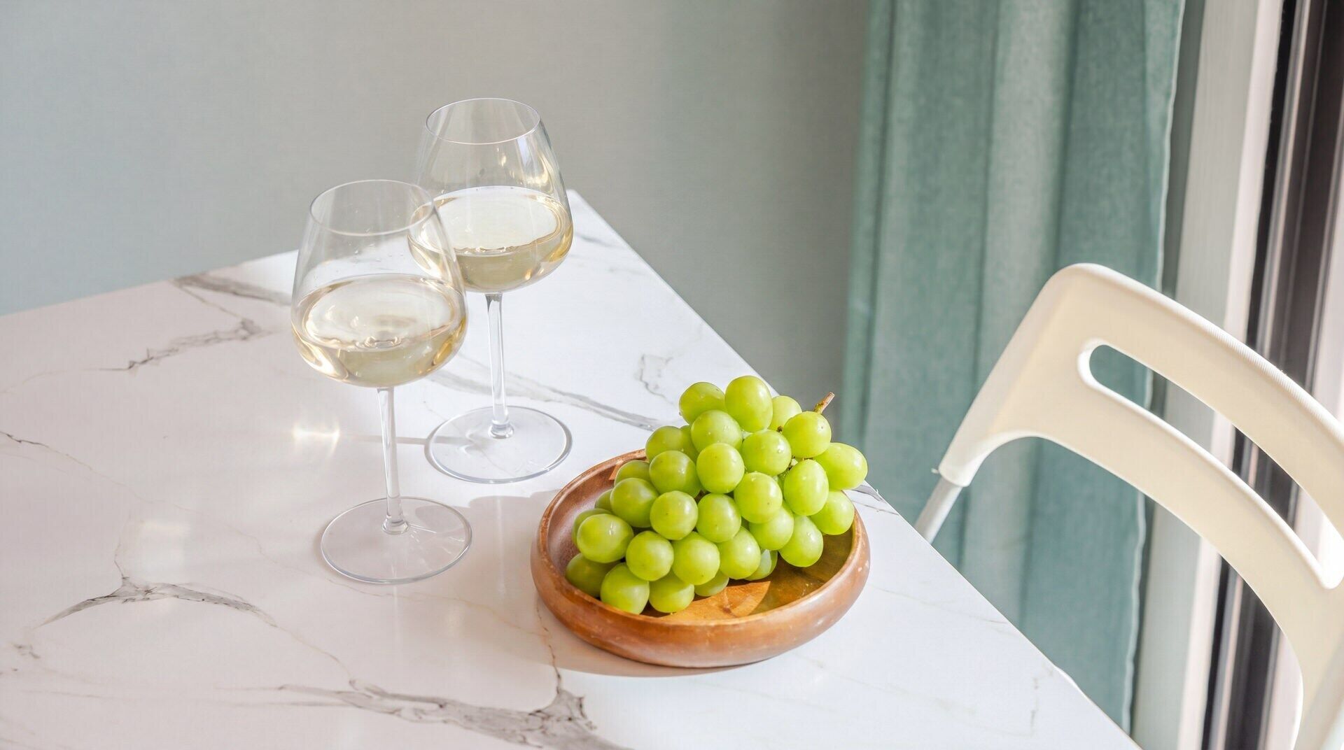 Ein Marmortisch mit zwei Weingläsern und einer Schale grüner Trauben.