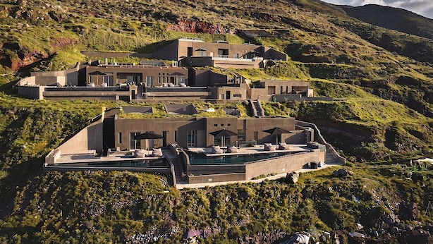 Un edificio moderno a più piani con piscina, situato su una collina circondato da natura.